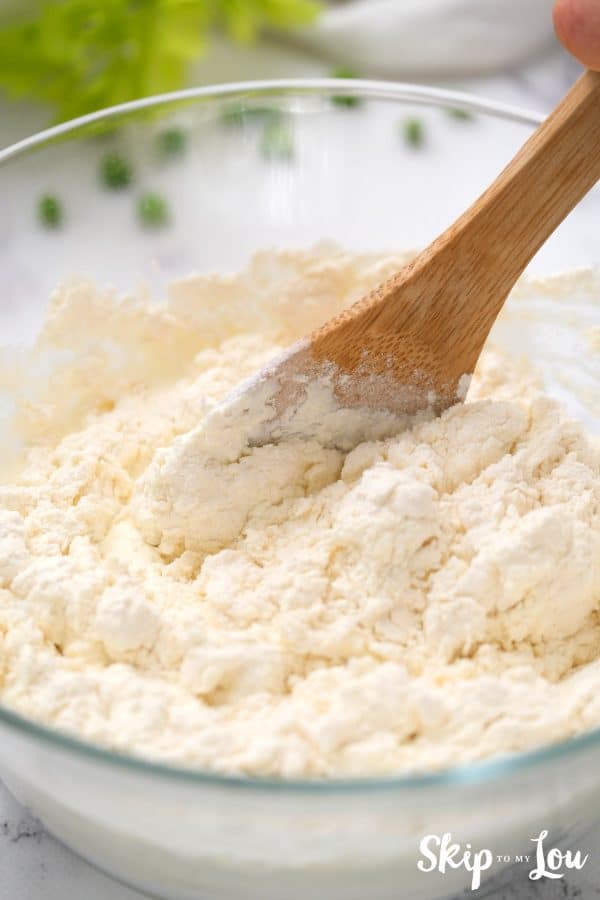 Wooden spoon mixing heavy cream with the flour mixture for the biscuits for the chicken pot pie. -Skip To My Lou