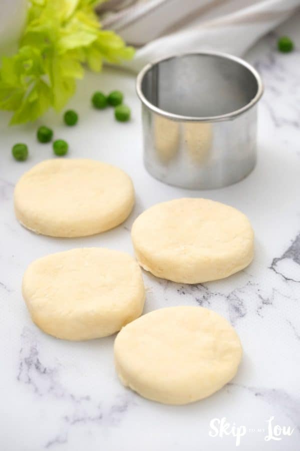 Round biscuits cut out of dough with a silver biscuit cutter for the chicken pot pie. -Skip To My Lou