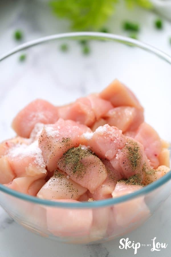 Raw chicken chunks seasoned with salt and pepper in a glass mixing bowl for the chicken pot pie. -Skip To My Lou