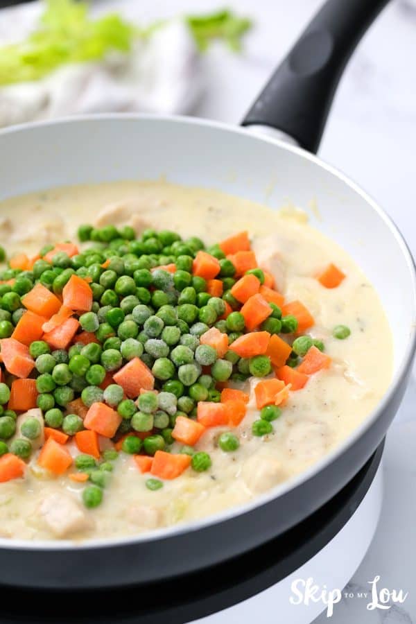 Peas and carrots added to creamy chicken mixture for the chicken pot pie in a skillet. -Skip To My Lou