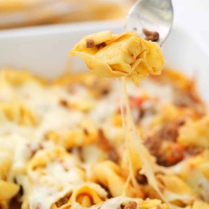 baked tortellini casserole served on white plate with a fork taking a bite out of it