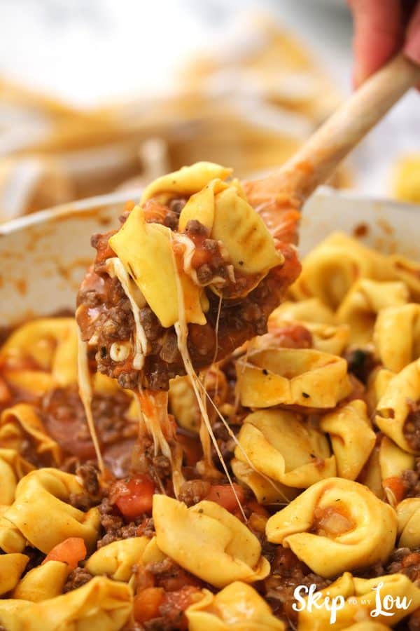 the tortellini is being stirred into the meat sauce in the skillet