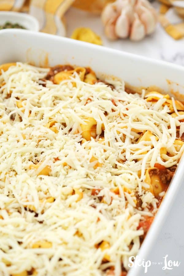 tortellini and meat sauce have been transferred to white casserole dish and covered with grated cheese
