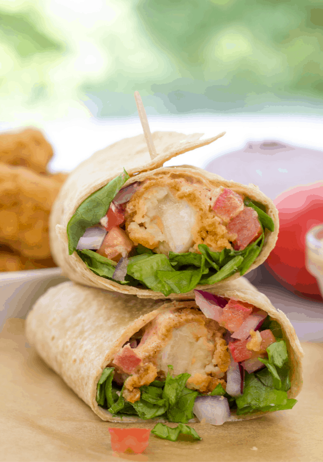 crispy chicken strip wrap cut in half sitting on parchment paper

