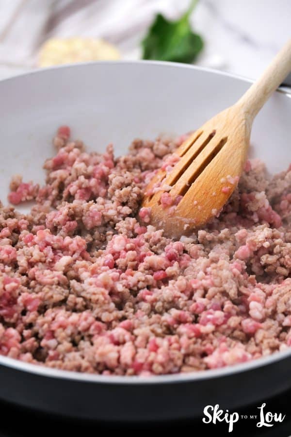 sausage being browned in non-stick skillet stirred with a slotted wooden spoon
