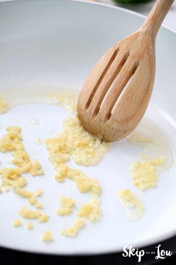 minced garlic sauteing in a non-stick skillet with a slotted wooden spoon stirring it