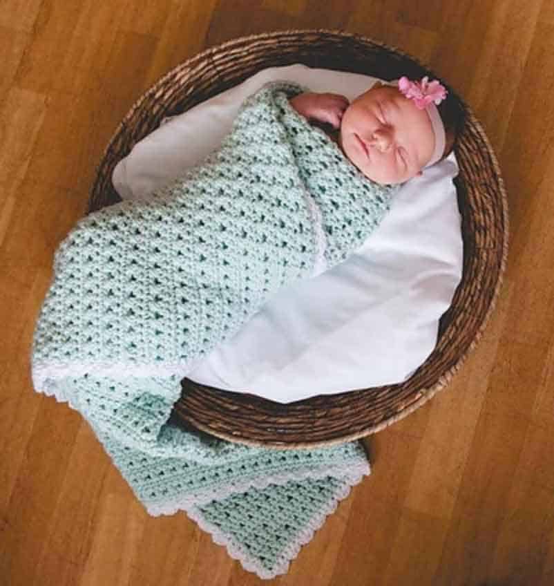 baby swaddled in mint green crochet blanket sleeping in basket