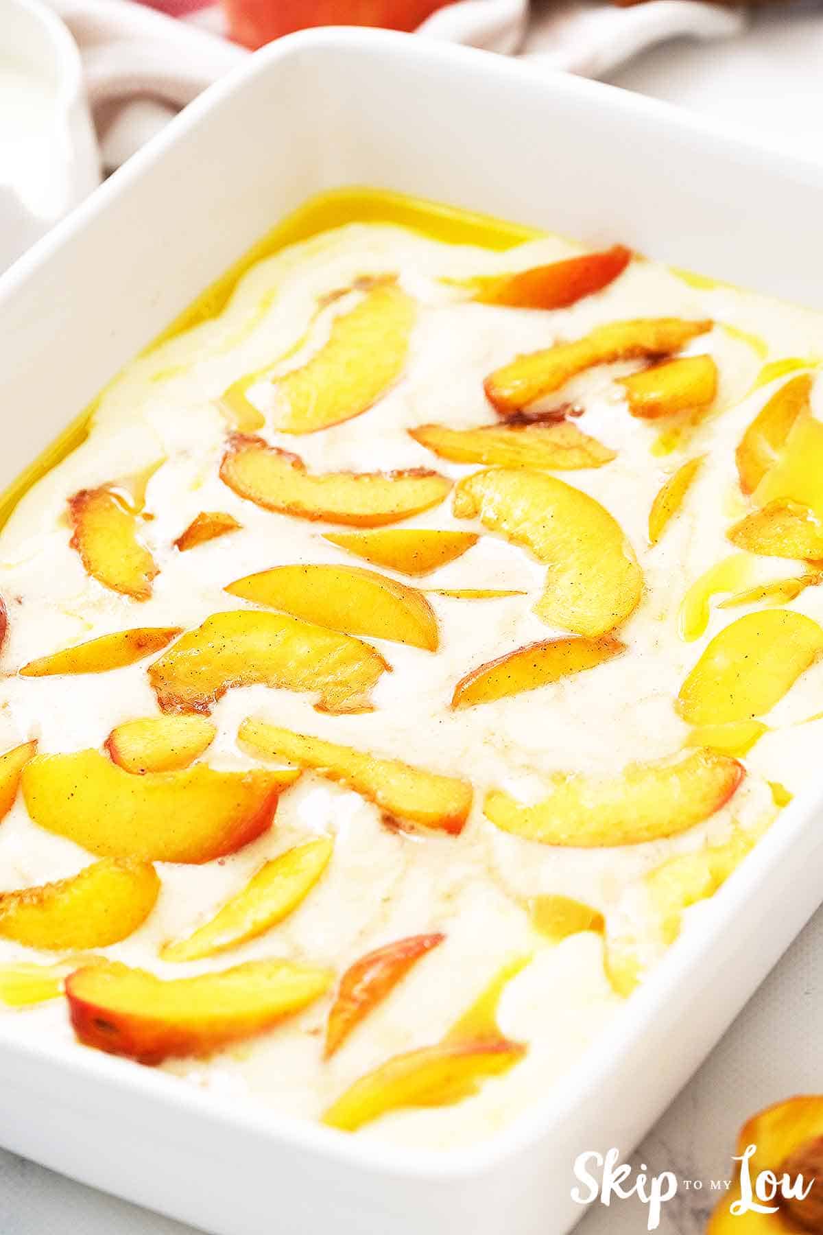 fresh peaches on top of batter and butter in white casserole dish