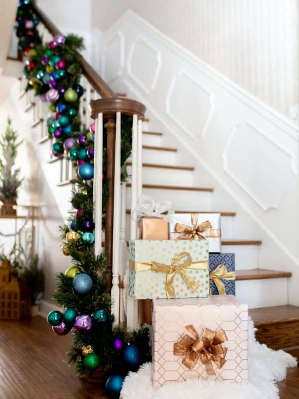 Image shows wrapped christmas presents next to stairs and other Christmas decoration.