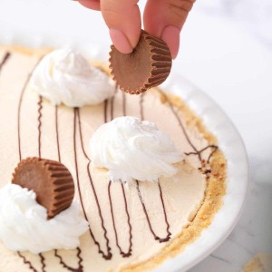 Adding peanut butter cup garnish on top of no bake peanut butter pie. -Skip To My Lou