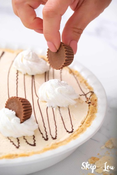 Adding peanut butter cup garnish on top of no bake peanut butter pie. -Skip To My Lou