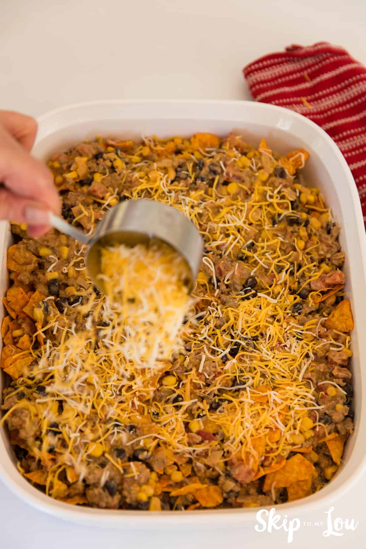 pouring cheese on top of Doritos casserole