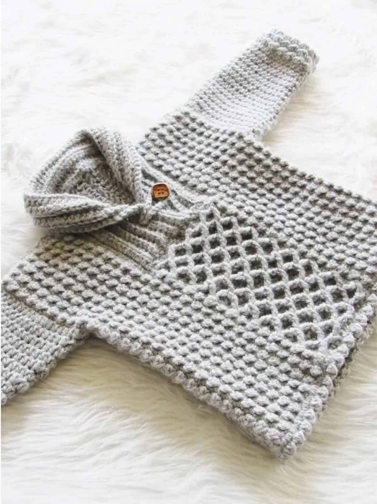 Image shows a gray baby boy pull over sweater laying on a white furry rug. -Skip To My Lou