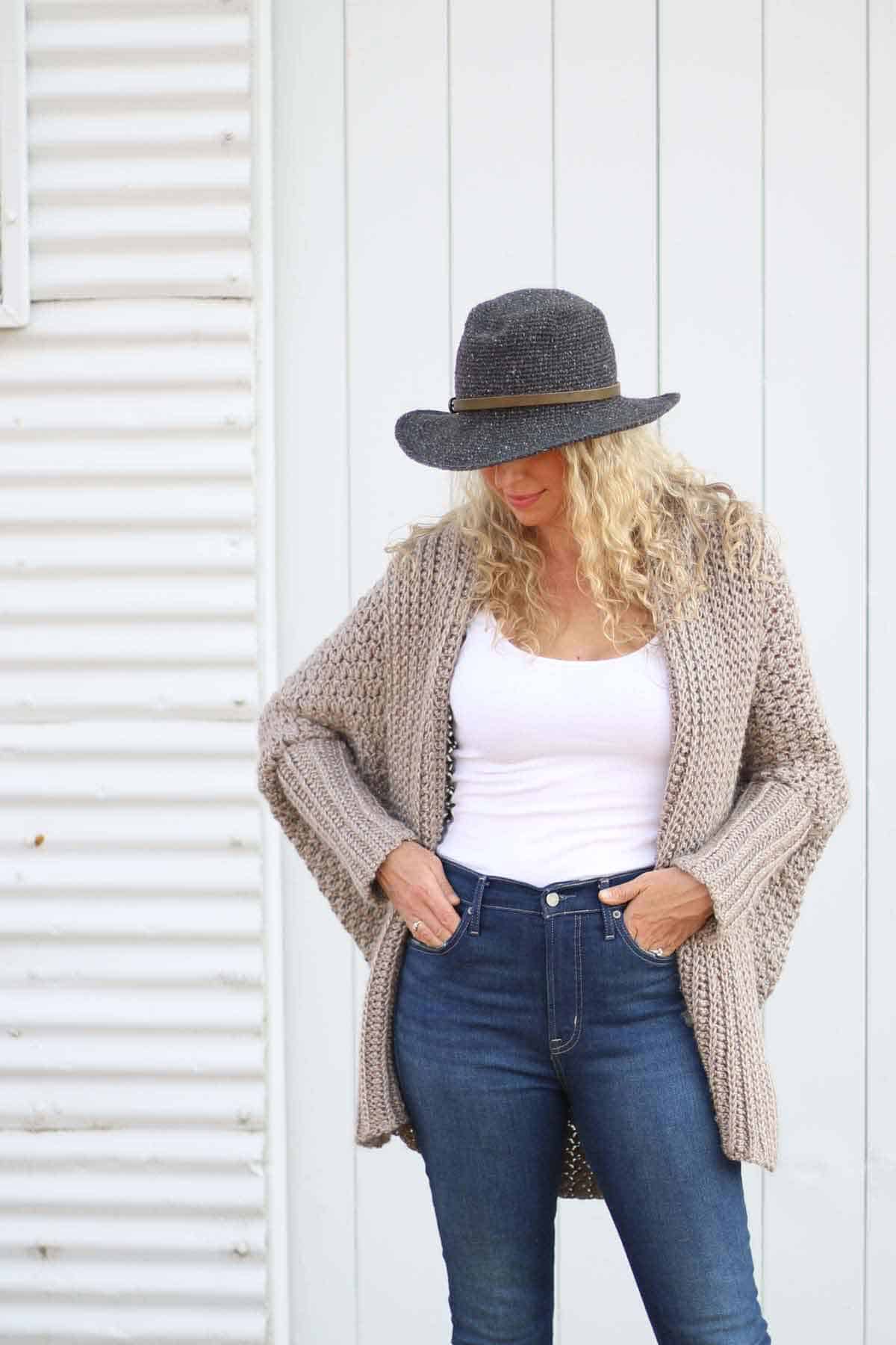 Woman wearing a rectangle crochet cardigan and a hat while looking down to the floor is shown. -Skip To My Lou