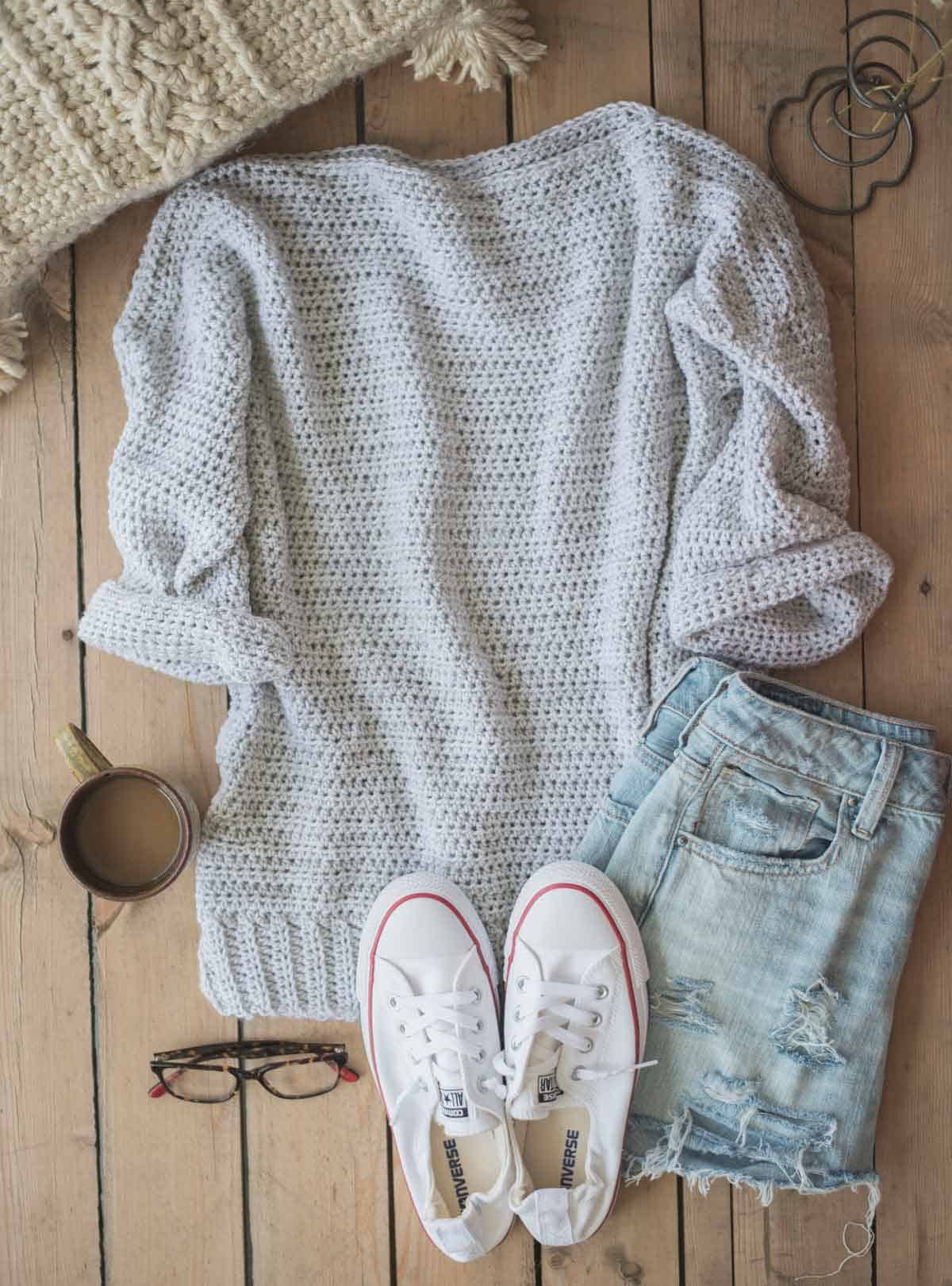 Image shows an oversized crochet sweater laying flat with jeans and tennis shoes at the side. -Skip To My Lou