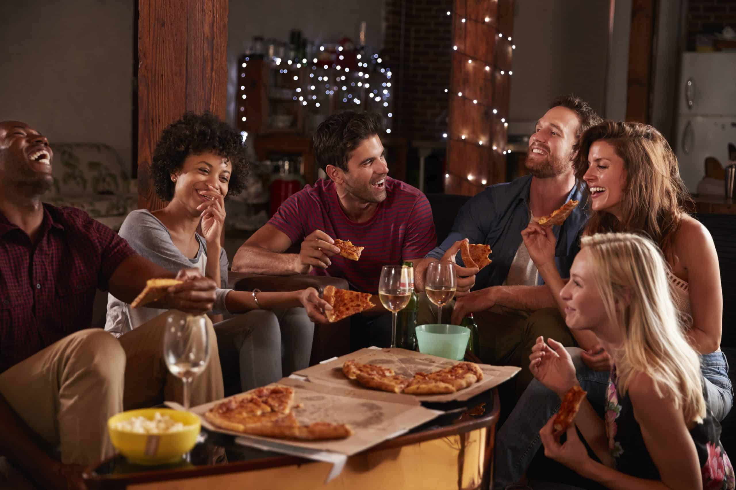 A group of people at a party eating pizza before playing the game Never Have I Ever