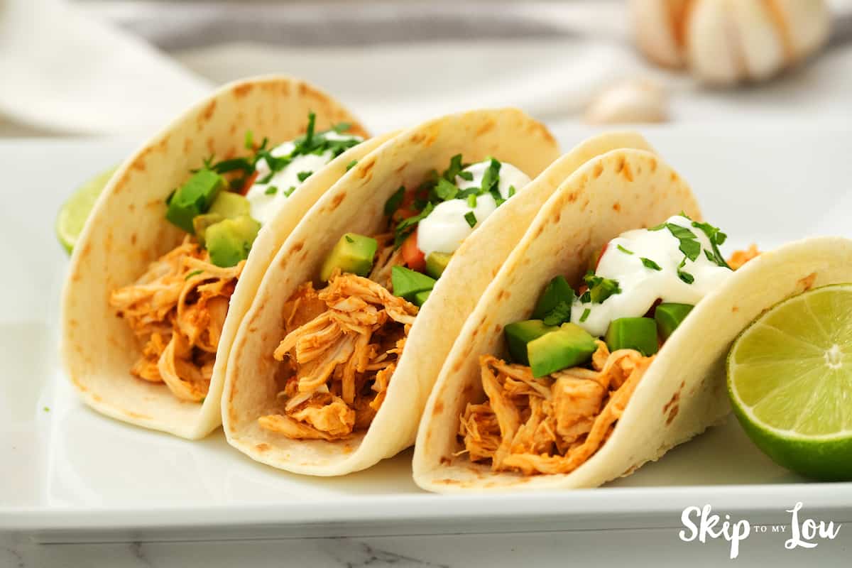 three shredded chicken tacos on a white plate with lime