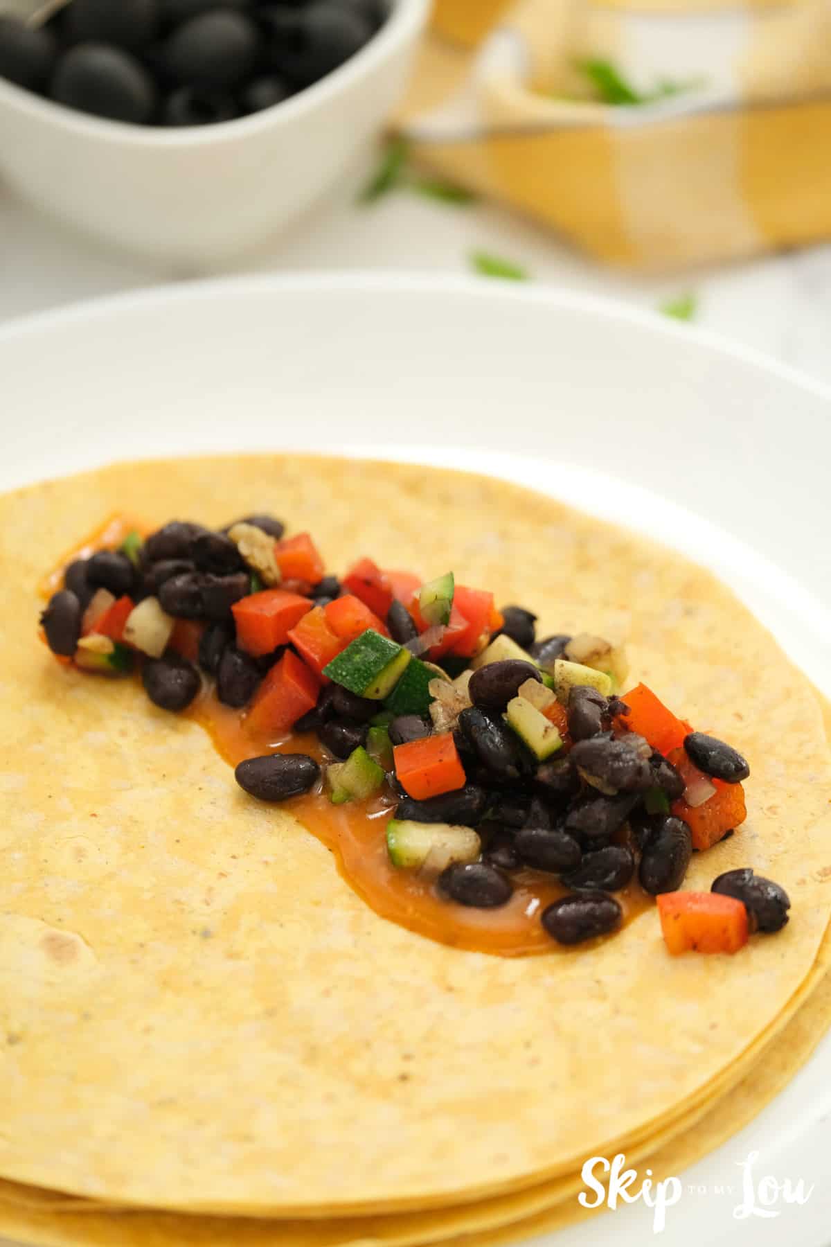 Next, spread some of the sauce over the tortilla, and add the filling. Roll and place lined up in a baking dish for your vegan enchilada recipe