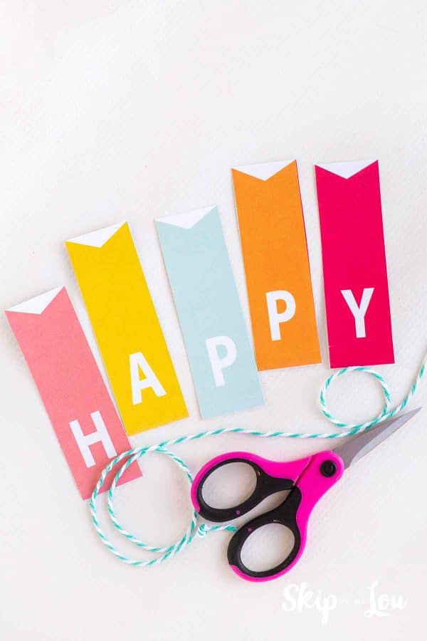 Letters spelling Happy, a blue and white cotton string and a pair of pink and black handled scissors by Skip to my Lou.