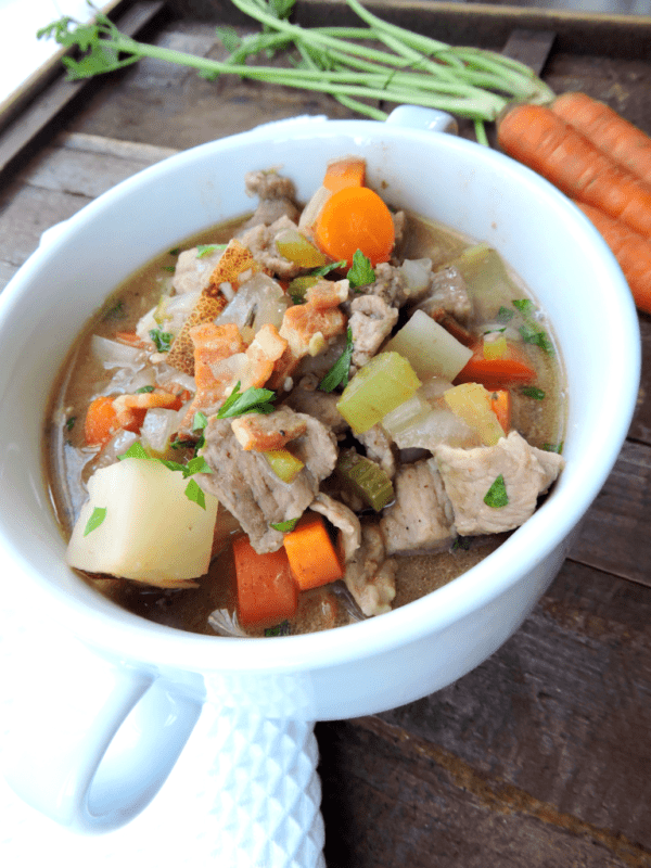 A white soup cup of hearty beef and bacon soup garnished with parsley