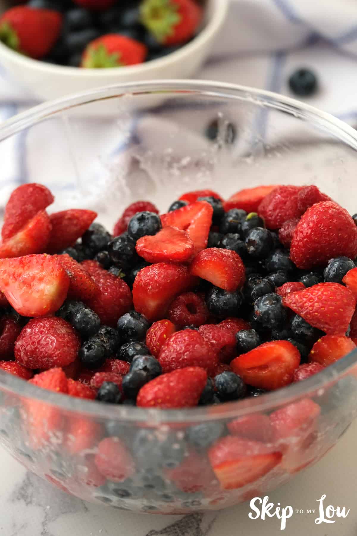 Berries soaking in a glass bowl in the cornstarch sugar mixture.