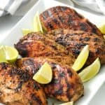 Jerk Chicken served on a white serving dish garnished with sliced limes. -Skip To My Lou