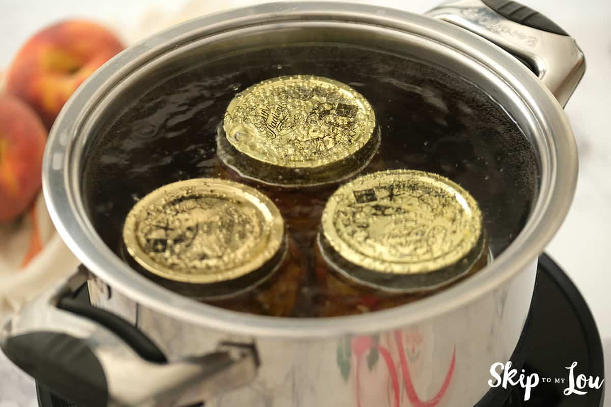 Canning jars with salsa inside and tightened lids in large pot filled with water ready to boil.