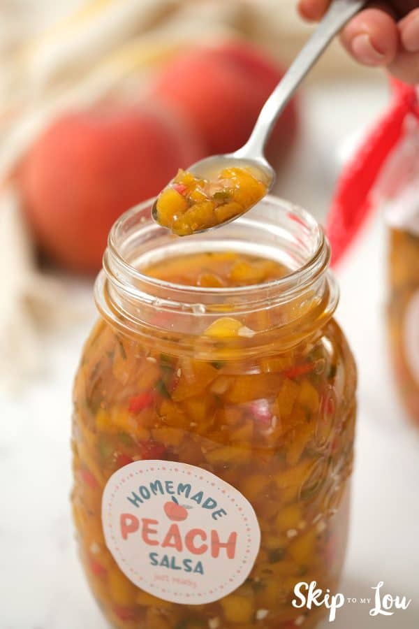 Jar of Peach Salsa with the lid off and a spoonful being taken out. Cute label on jar Homemade Peach Salsa