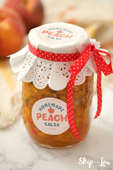 Peach salsa in a canning jar with homemade peach salsa label, white lace top, red and white ribbon.