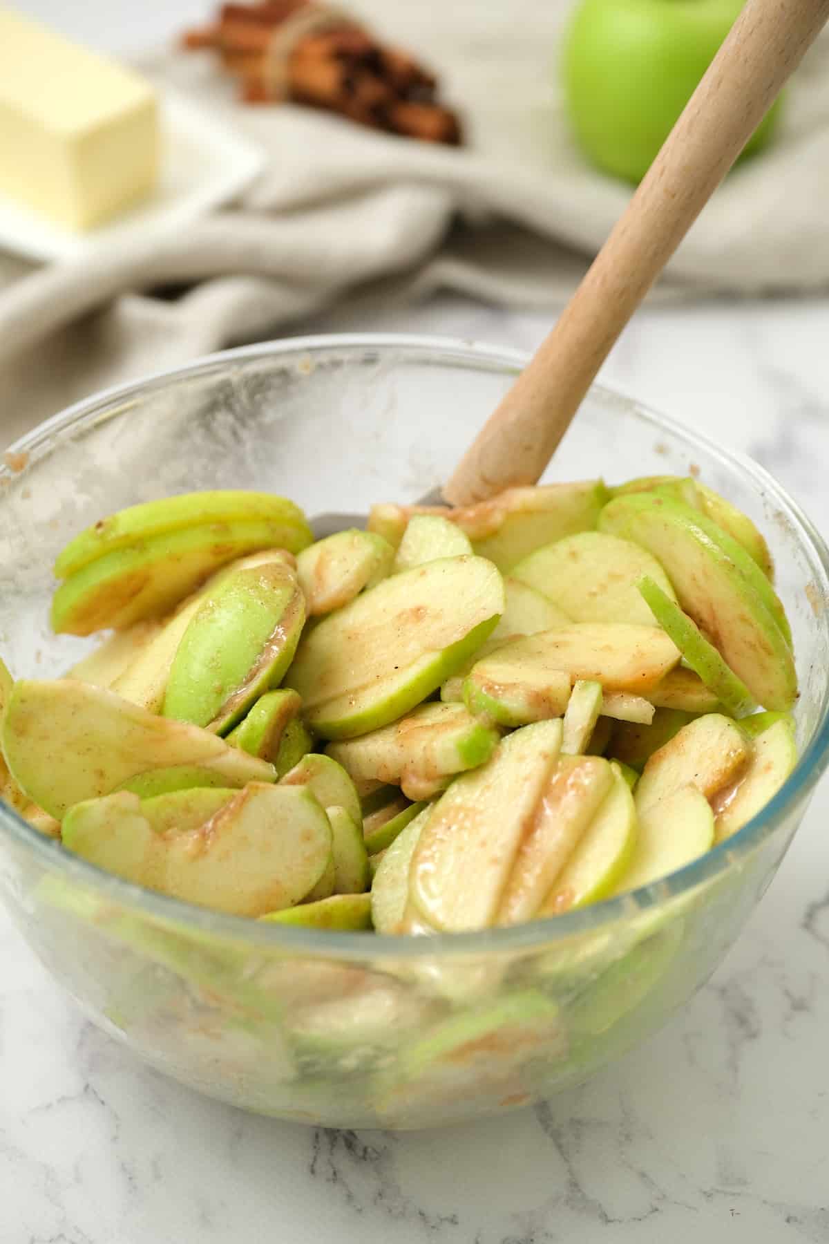 Apple slices tossed with the dry ingredients for the apple pie filling in a large glass bowl.