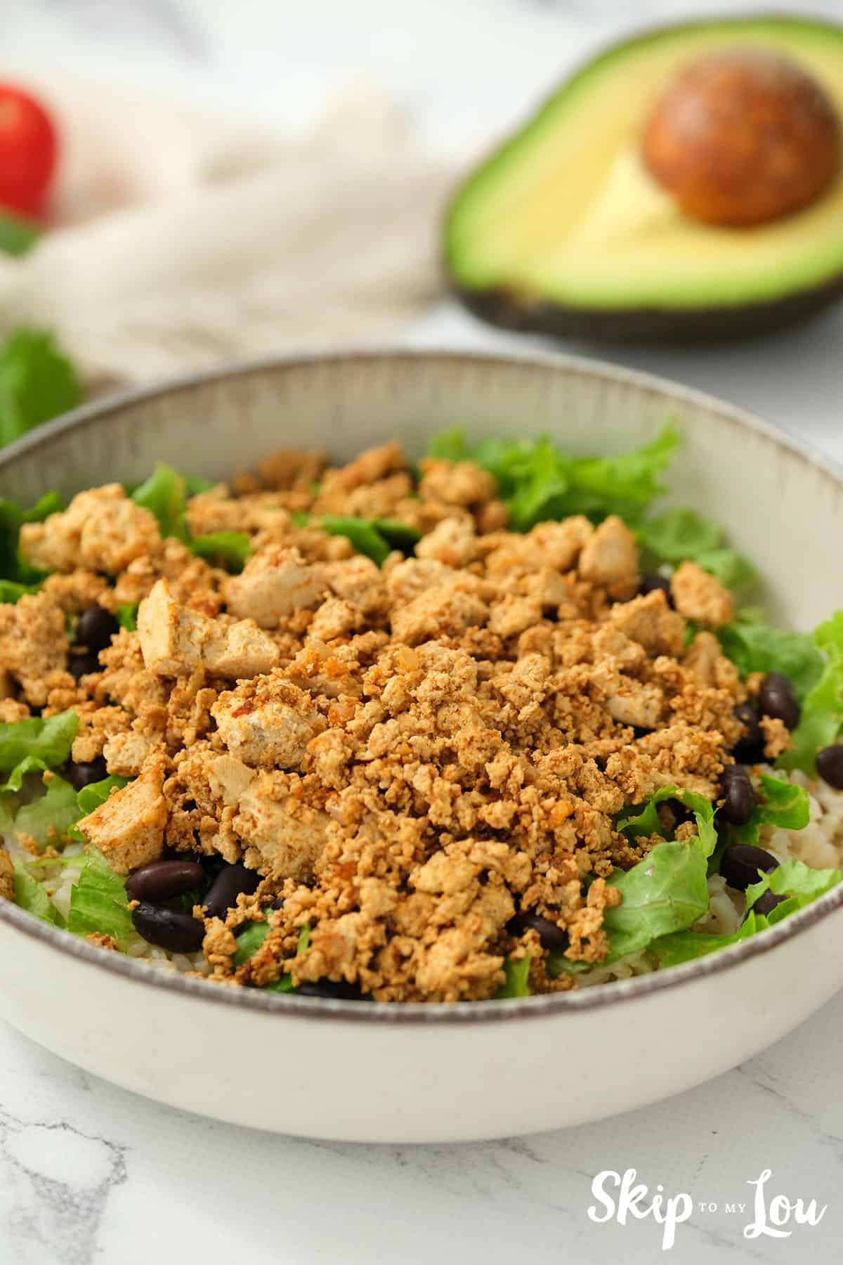 Tofu added to the sofritas bowl on top of the lettuce and black beans in a white serving dish.