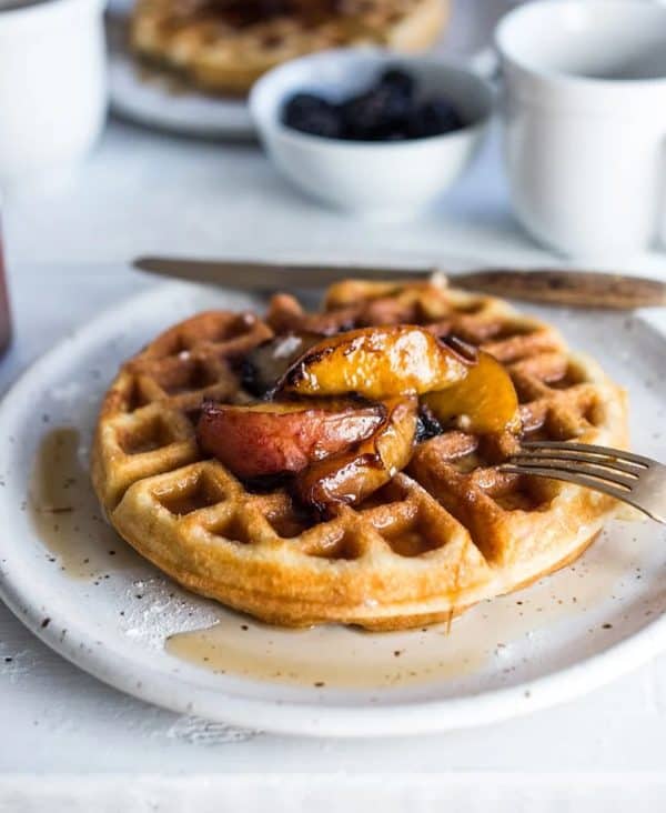 Image shows a sourdough waffle with apple on top served on a plate.