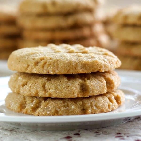 Image shows three peanut butter cookies made with sourdough on top of a white plate, with some other cookies on the background.