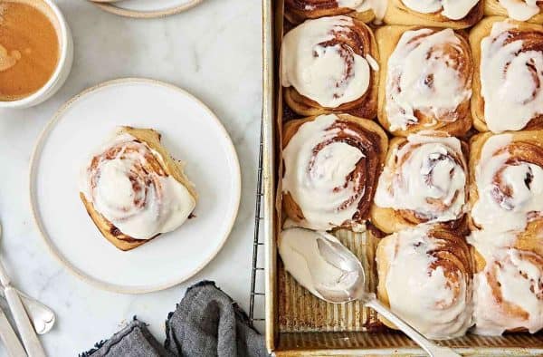 Image shows a batch of sourdough cinnamon buns, one of them is served on a plate.