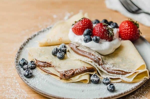 Image shows two sourdough crepes served with bleuberries and heavy cream and nutella.