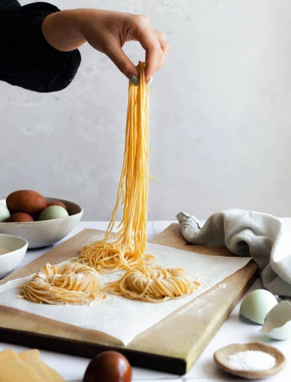 Image shows a homemade pasta made with sourdough, and a hand holding it .
