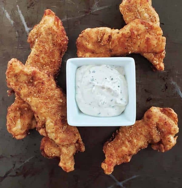 Image shows four fried chicken  stripes with sourdough and a sauce served in the middle.