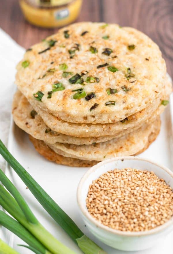 Image shows scallion pancakes on top of each other with sesame seeds next to it.