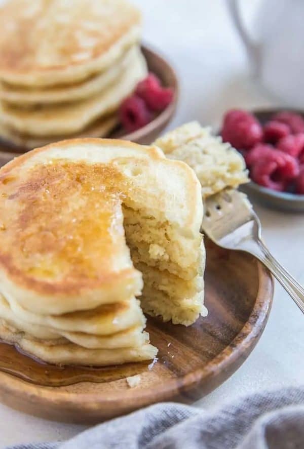 Image shows a pile of sourdough pancakes with raspberries next to it.