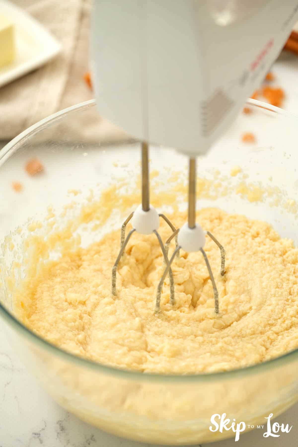 Batter for Toffee Doodle Cookies mixed with a hand mixer in a large clear mixing bowl. -Skip To My Lou