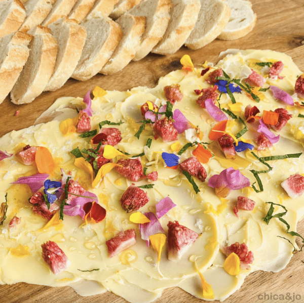 Image shows a butter charcuterie board with toppings on it and several slices of bread next to it.