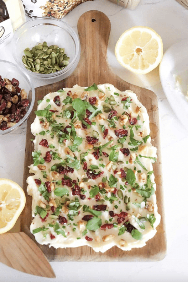Image shows a butter charcuterie board with toppings and half-cut lemons next to it.