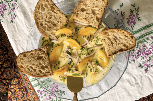 Image shows a glass cake stand with butter and bread on it to create an elegant butter charcuterie board.