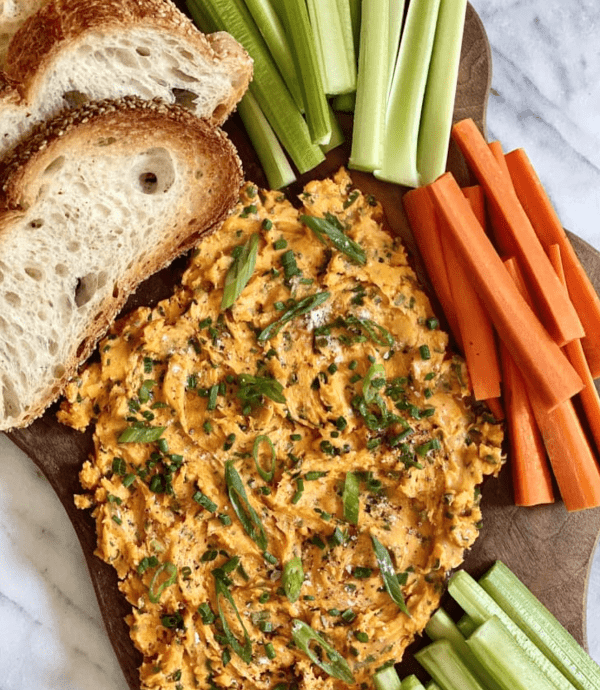 Image shows a buffalo-ranch butter board with celery and carrot sticks next to it, as well as some bread slices.