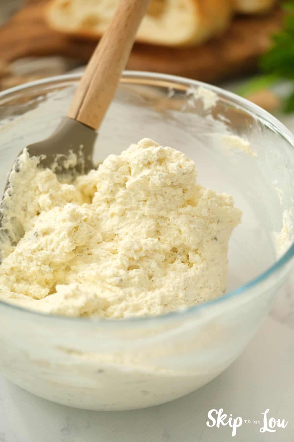 Glass mixing bowl with cream cheese, butter, ranch dressing mix, and parmesan cheese stirred together with wooden spoon. Herb Butter Spread Recipe -Skip To My Lou