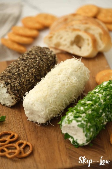 Herb butter cheese spread sliced and served on a wooden board with bread, crackers, and pretzels.