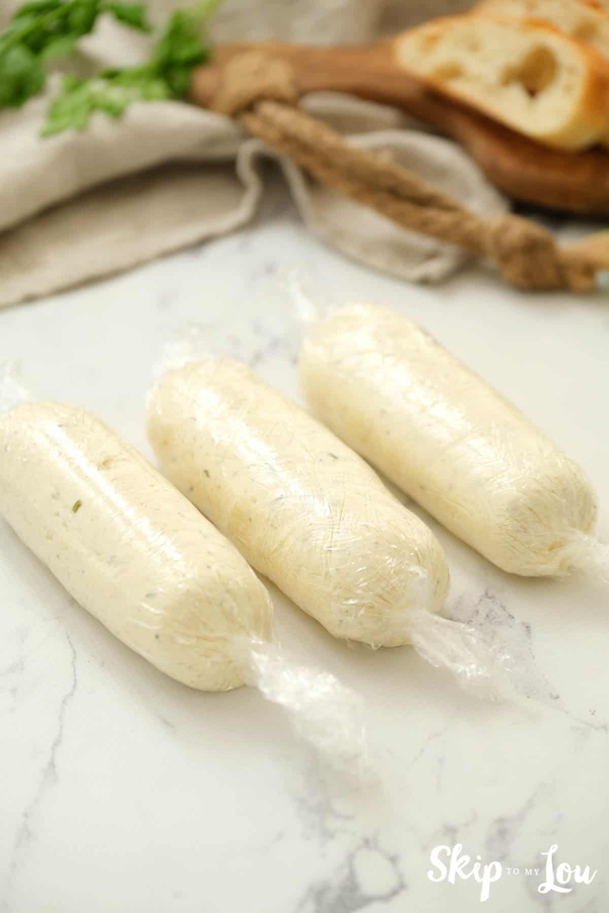 Herb Butter Spread formed into three logs wrapped in plastic wrap. -Skip To My Lou