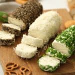 Herb butter spread sliced and served on a wooden board with pretzels and crackers. -Skip To My Lou