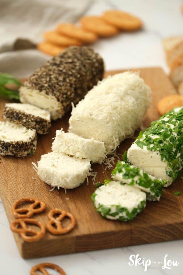 Herb butter cheese spread sliced and served on a wooden board with pretzels and crackers. -Skip To My Lou