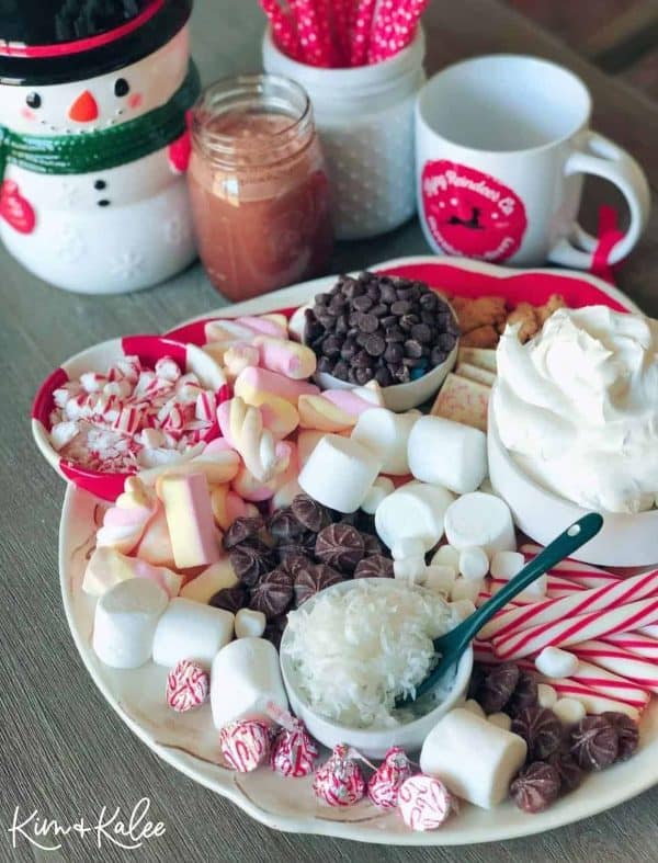 Image shows a hot chocolate charcuterie board with cocoa, chocolate chips, marshmallows, etc. via Kim & Kalee